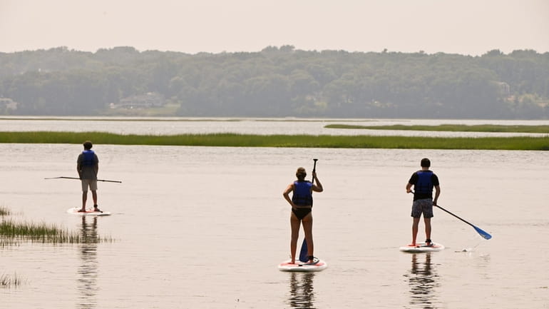 Paddle boarders in the waters of Stony Brook Harbor in...