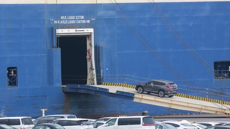 Cars for export are loaded onto a cargo ship at...
