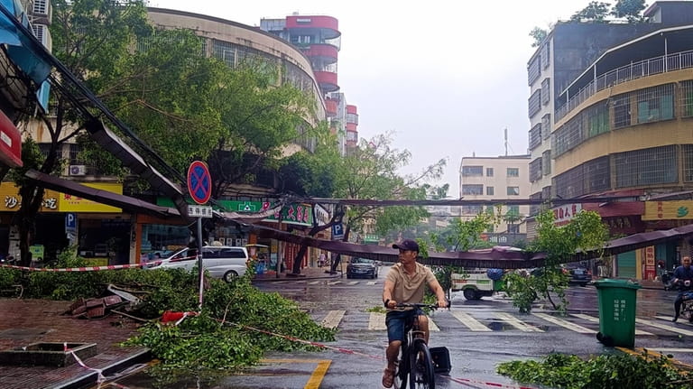 A cyclist rides past fallen debris and trees in the...