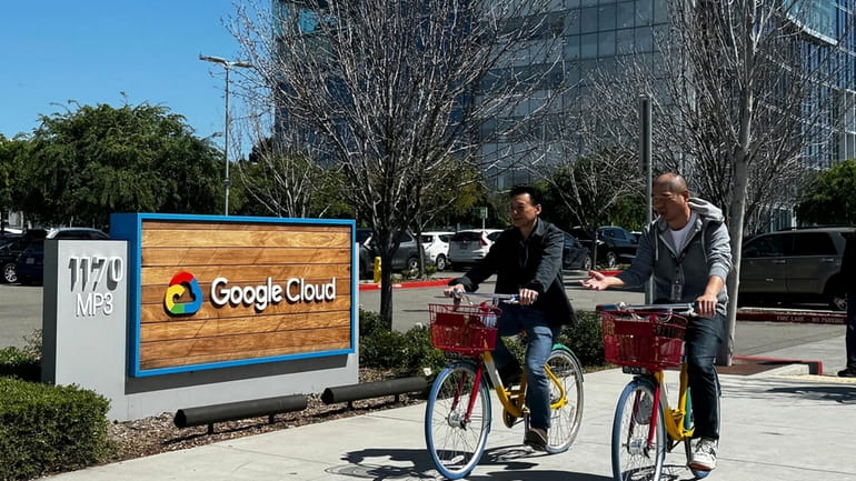 Two people ride past the Google sign outside the Google...