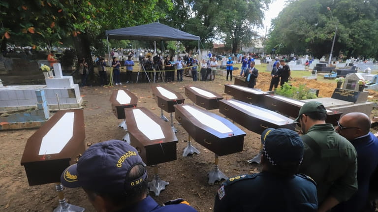 Authorities stand next to the nine coffins that contain the...