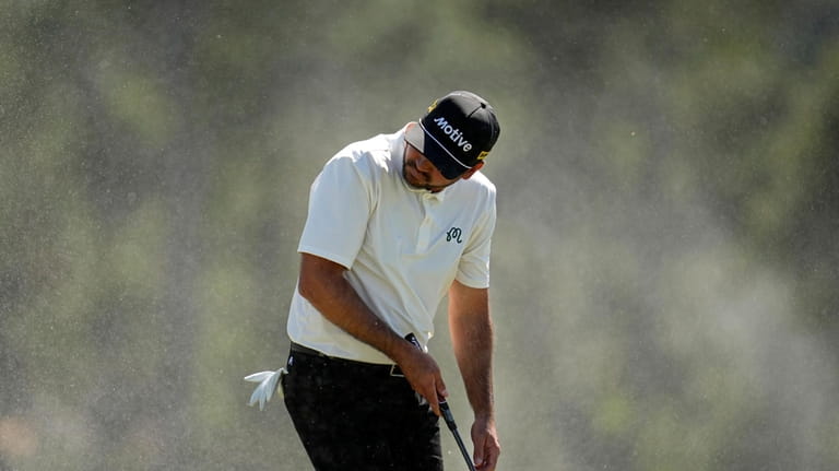 Jason Day, of Australia, shields himself from blowing sand on...