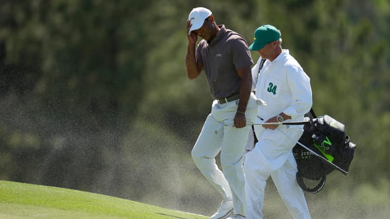 Tiger Woods and caddie Lance Bennett shield, their faces form...