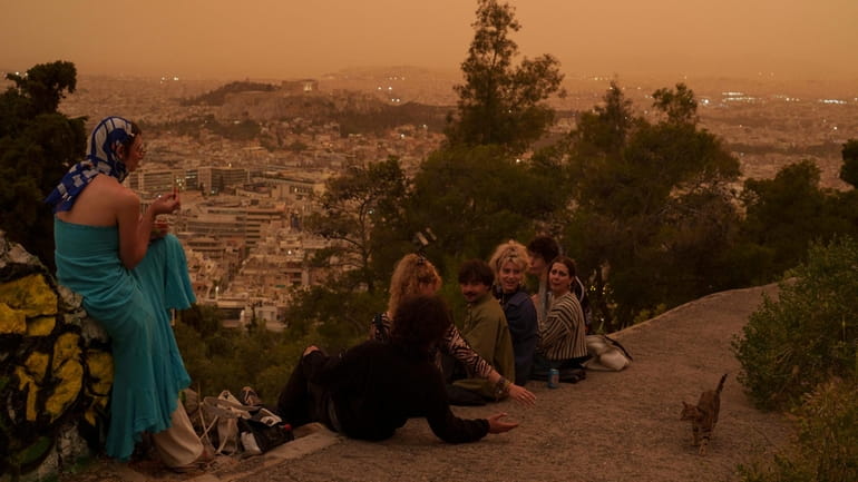 Tourists play with a cat at Lycabettus hill as the...