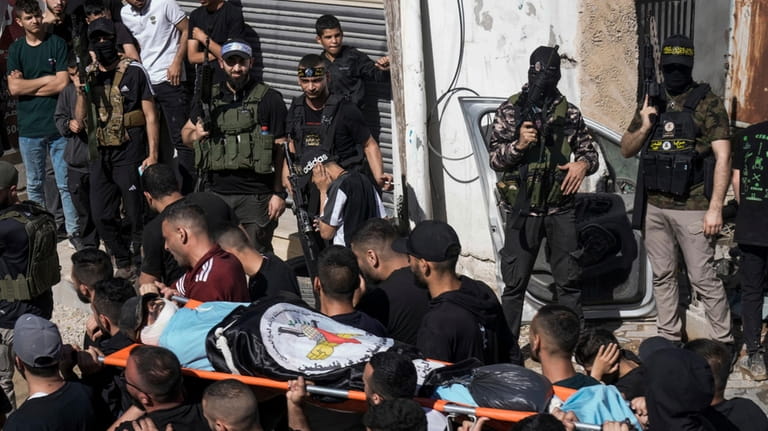 Palestinian gunmen fire into the air as mourners carry the...