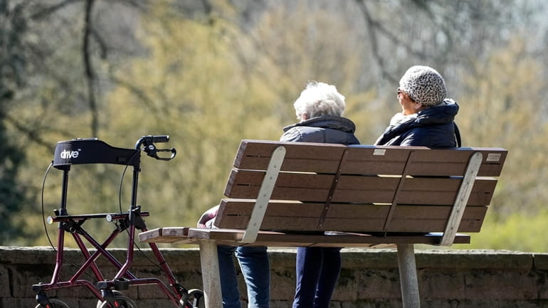 Elderly women sit on a bench beside their walker in...
