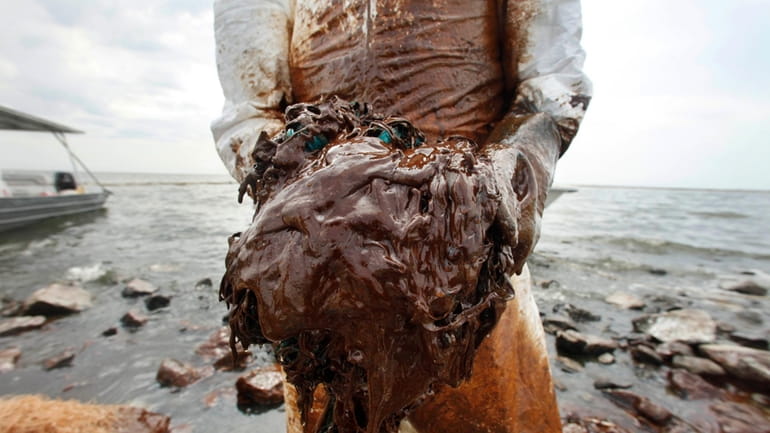 A cleanup worker picks up blobs of oil in absorbent...