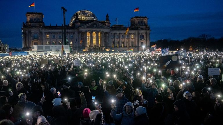 People hold up their cell phones as they protest the...