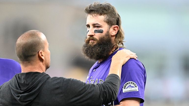 An unidentified trainer, left, looks at Colorado Rockies' Charlie Blackmon,...