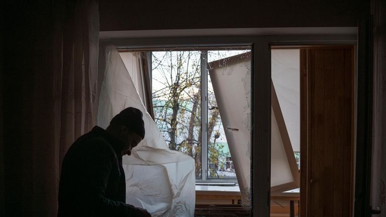 A man uses plastic to cover a broken window in...