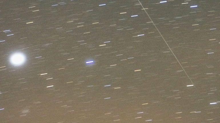 A Geminid meteor streaks diagonally across the sky against a...