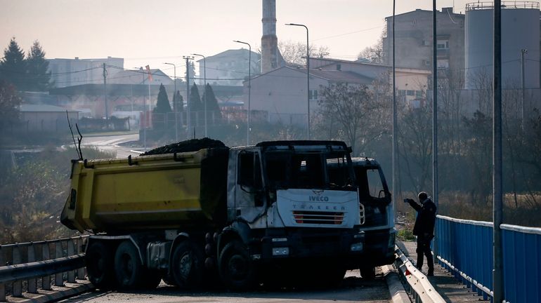 A man takes photos of a burnt-out truck, part of...