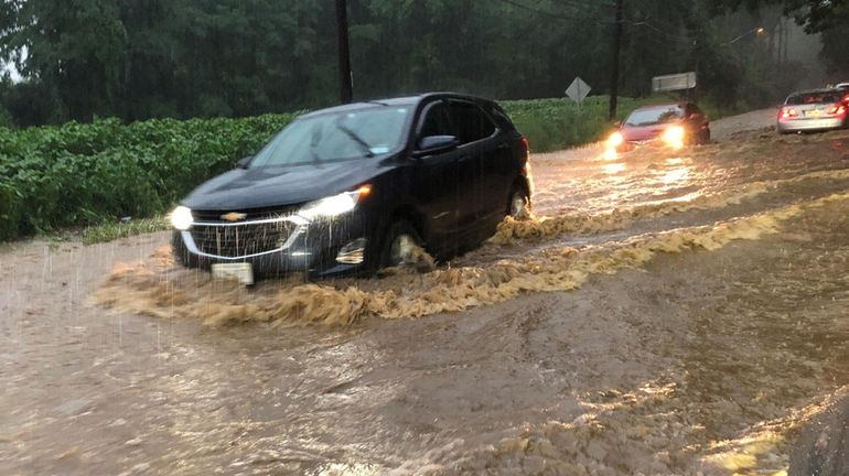 A car makes its way through a flooded section of...