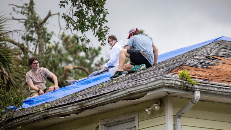 Residents repair their roof as high winds from an outer...