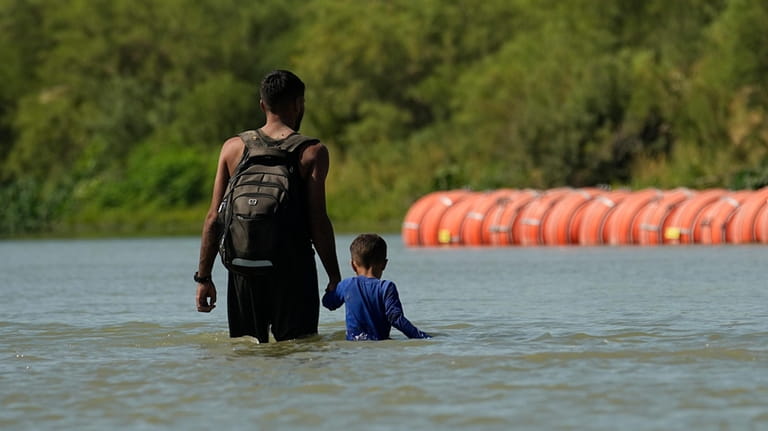 Migrants walk past large buoys being used as a floating...