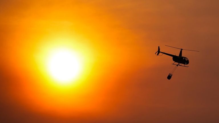 A helicopter carries a bucket as it flies over homes...