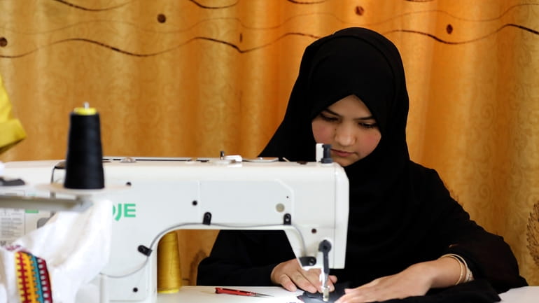An Afghan woman tailor works with a sewing machine in...