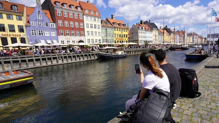 Two tourists sit watching sightseeing ferries sail by in Copenhagen’s...