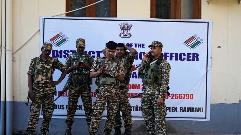 Security personnel members stand and wait as polling officials prepare...