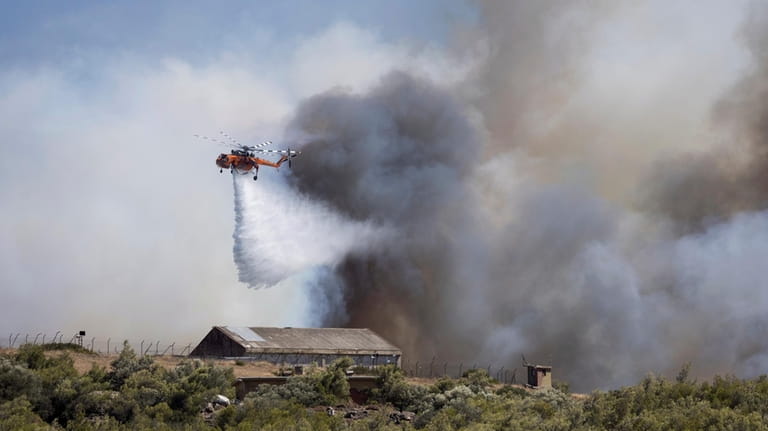 A firefighting helicopter drops water over a wildfire at Keratea...