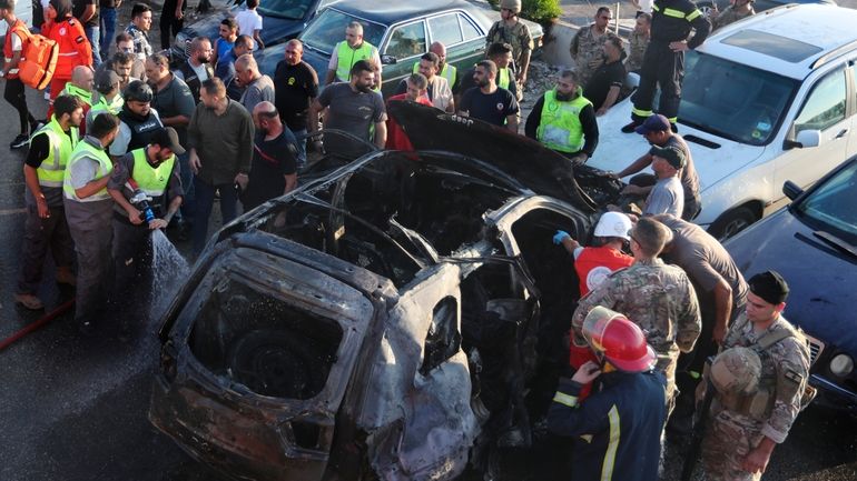 Civil Defence workers extinguish a car that hit by an...