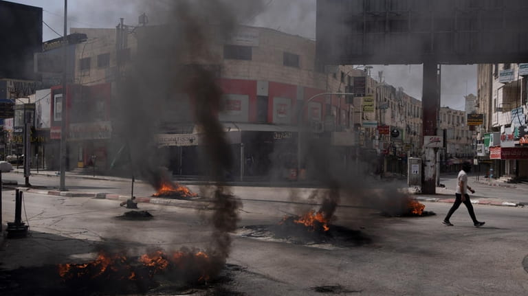 A Palestinian man walks past burning tires during clashes with...