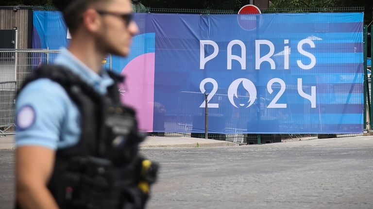 A police officer walks past a Paris olympics canvas at...