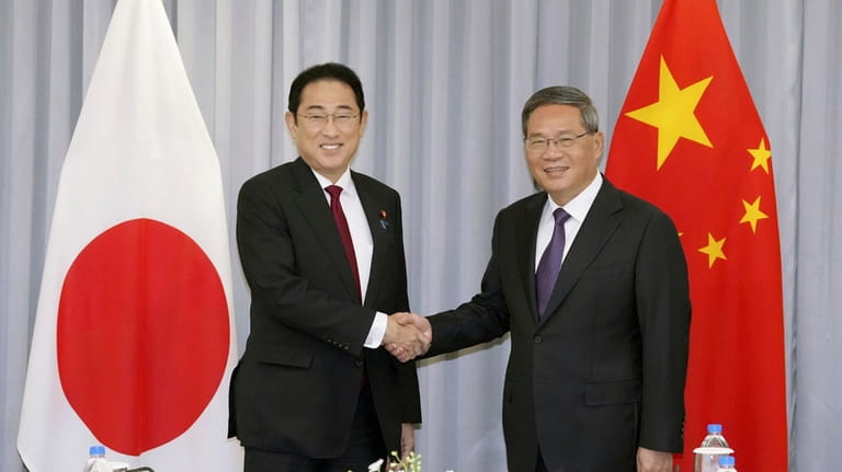 Japanese Prime Minister Fumio Kishida, left, shakes hands with Chinese...