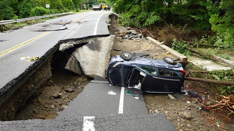 A damaged car lays on a collapsed roadway along Route...