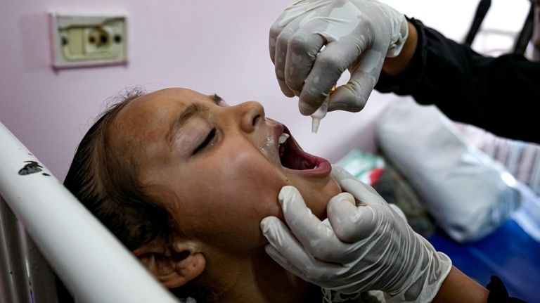 A health worker administers a polio vaccine to a child...