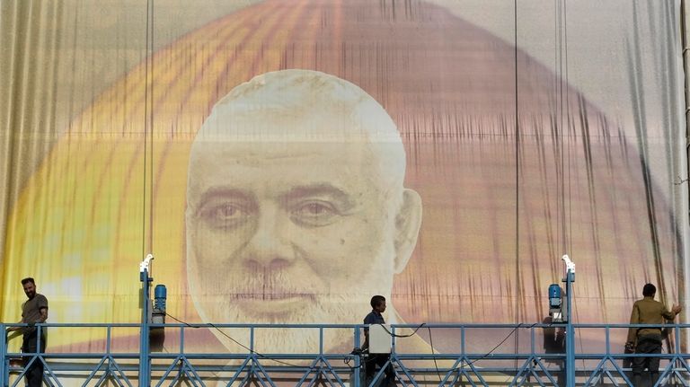 Iranian workers install a huge banner on a wall showing...