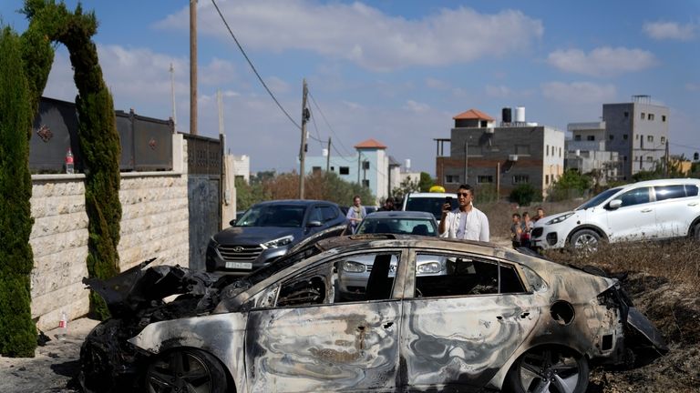 A Palestinian films a torched vehicle, seen the morning after...