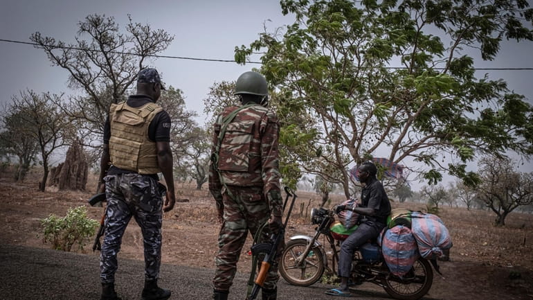 A police officer and a soldier from Benin stop a...