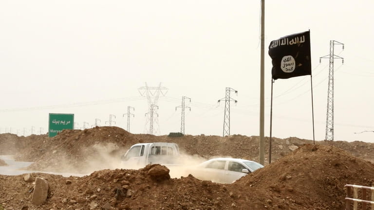 Islamic State militants pass a checkpoint bearing the group's trademark...