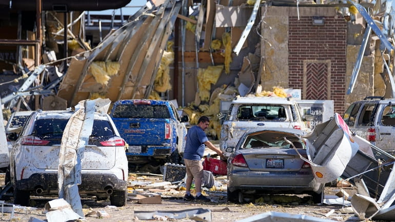 A man looks at a damaged car after a tornado...