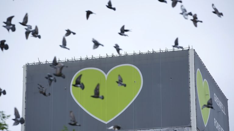 A flock of pigeons fly past the remains of Grenfell...