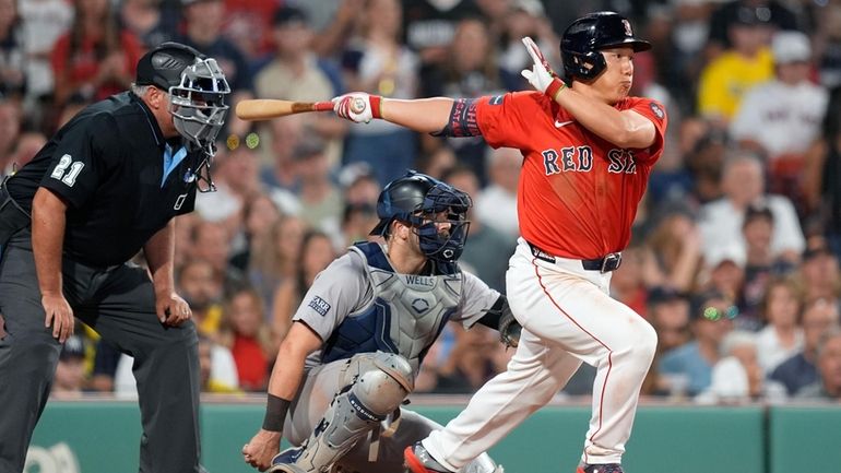 Boston Red Sox's Masataka Yoshida, right, follows through on his...