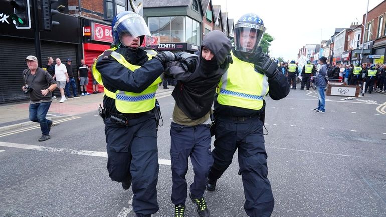 A man is detained by police officers as people protest...