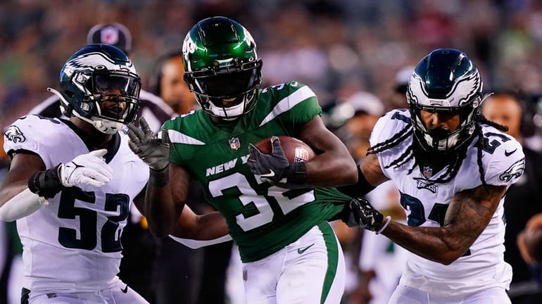 New York Jets' Michael Carter runs with the ball between...