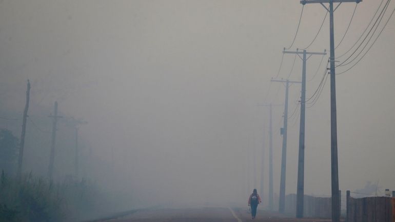 A person walks on the BR-319 highway through smoke from...