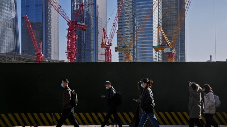 People wearing face masks walk by construction cranes near office...