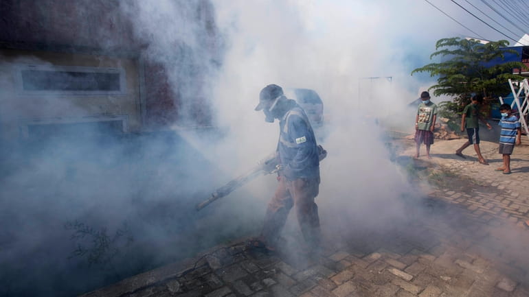 A worker fumigates a neighborhood with anti-mosquito fog to control...