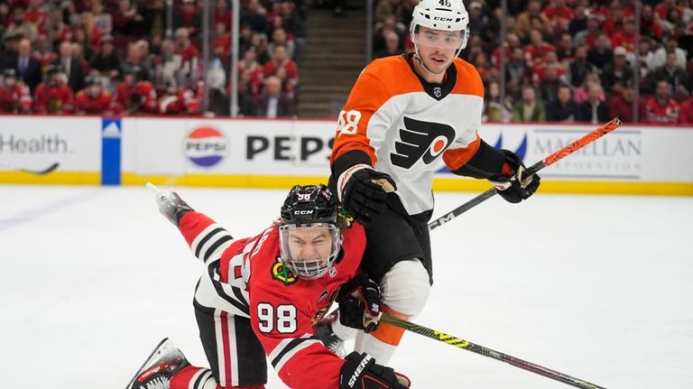 Chicago Blackhawks center Connor Bedard, left, trips over Philadelphia Flyers...