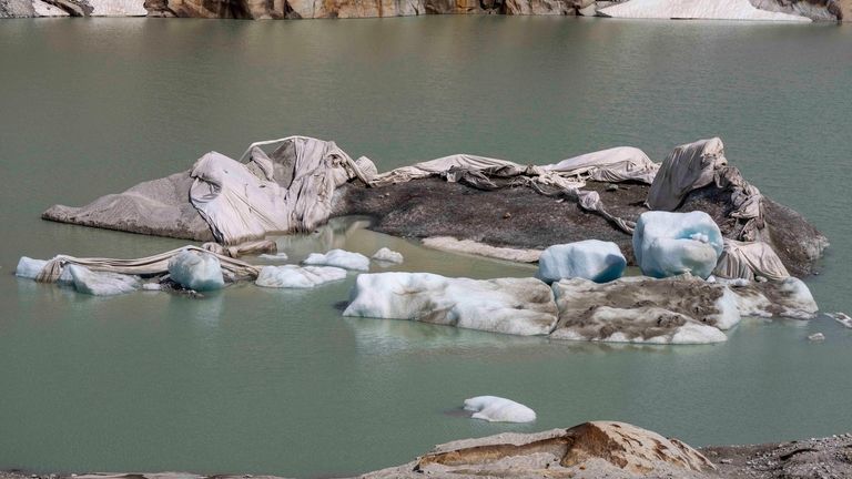 Chunks of ice float in a lake in front of...