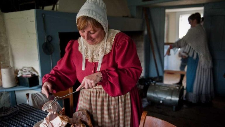 Joanne Graves, in period dress, cuts up a freshly roasted...