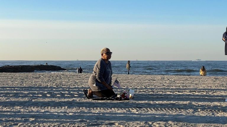 JoAnn Delgado kneels at Point Lookout Memorial Park as people gather...