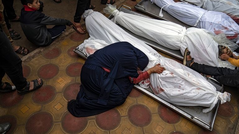 A woman mourns the covered bodies of her child and...