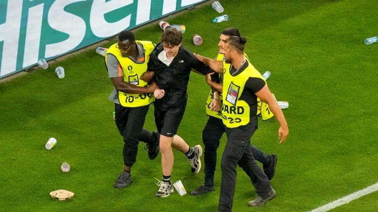 A pitch invader is taken away while spectators throw plastic...