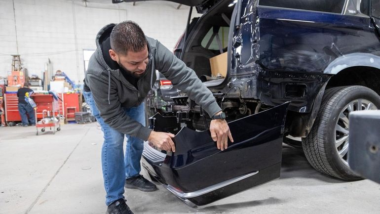 Shop foreman and manager Eddie Torres examines an SUV's bumper...