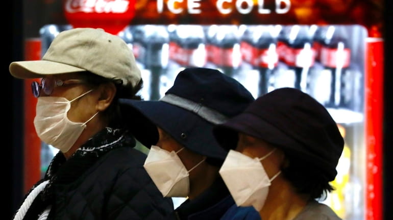 Tourists from Korea wearing protective masks walk with their belongings...